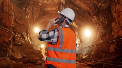 back view of asian male engineer with safety helmet talking on smartphone while standing in underground mine tunnel