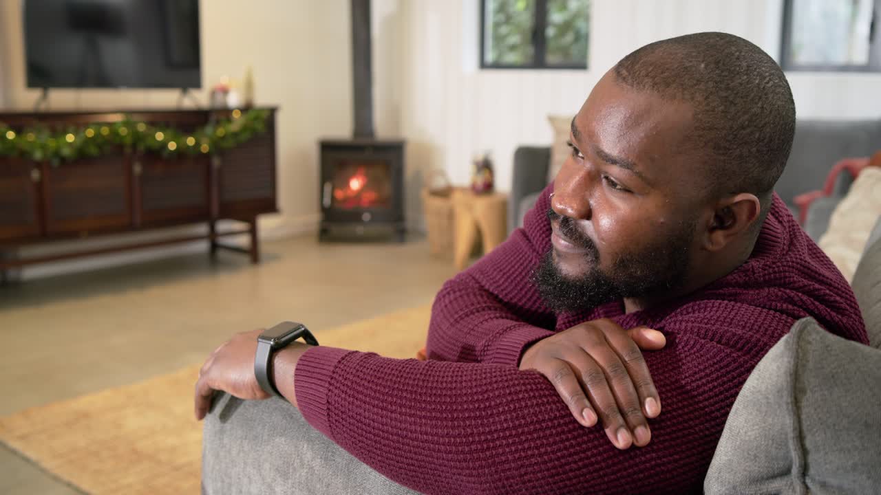 Mid adult African American man on gray sofa following gaze shift turning head toward camera smiling