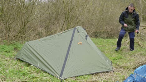 An-outdoorsman-tying-down-his-tent-to-secure-it-from-the-elements-while-camping-at-Thetford-forest-in-United-Kingdom