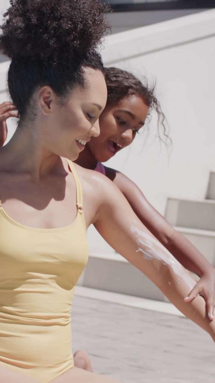 Vertical video: Woman and girl in swimsuits showing arm cream, girl rubbing cream for sun by pool
