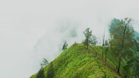 misty clouds roll gently over trunyan hill, surrounded by vibrant green mountains captured by drone, revealing a serene and peaceful tropical scene in bali’s highlands