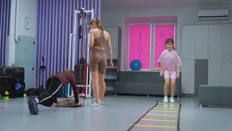 sesión de entrenamiento con un entrenador que supervisa a niñas jóvenes que participan en diferentes actividades de acondicionamiento físico, incluidos ejercicios de equilibrio y ejercicios de agilidad, en un entorno de gimnasio moderno con equipos de entrenamiento
