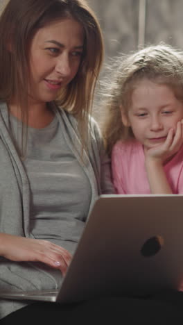 woman shows little children funny videos on modern laptop. toddler and preschooler look at screen of device on lap of mom in wheelchair closeup