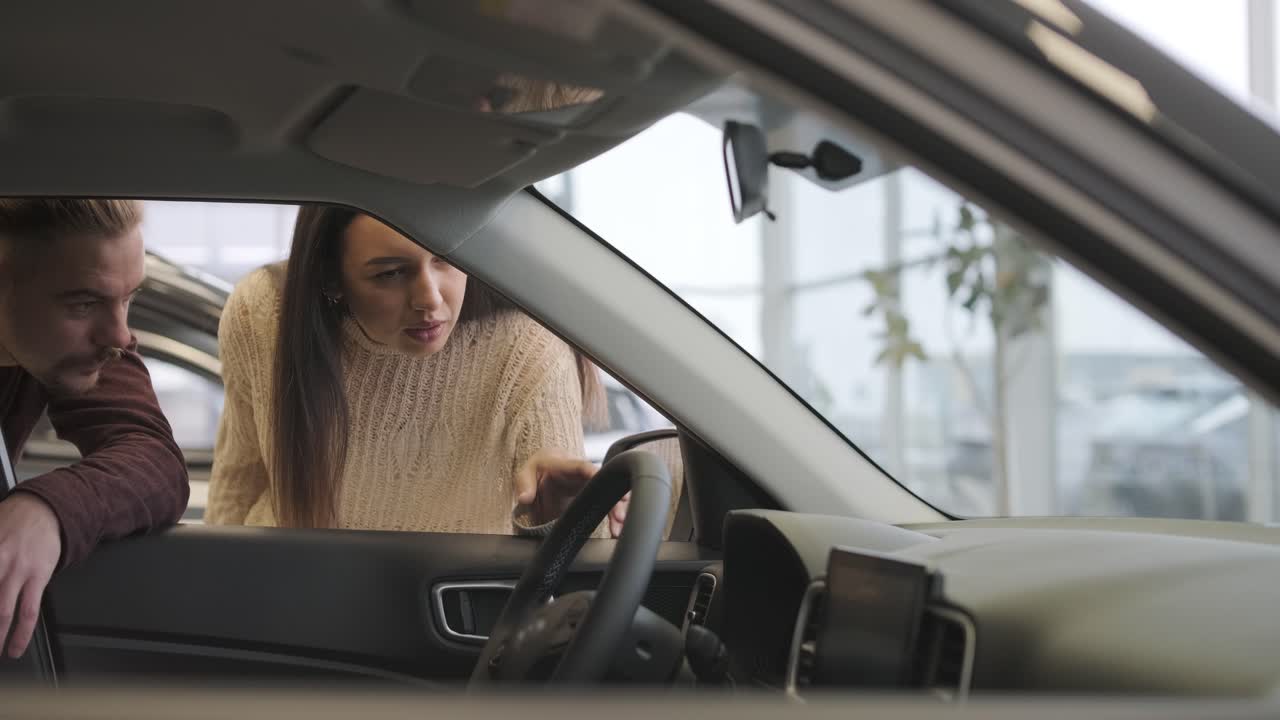 una hermosa pareja de jóvenes en la sala de exposición de automóviles eligiendo un coche nuevo para comprar.