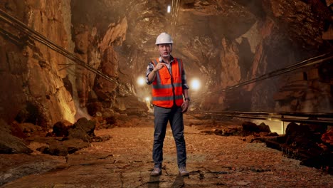 full body of angry asian male engineer with safety helmet shouting at someone while standing in underground mine tunnel