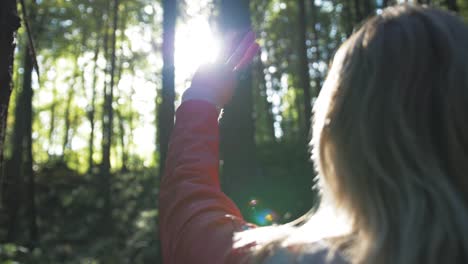 woman reaching towards sunlight in forest