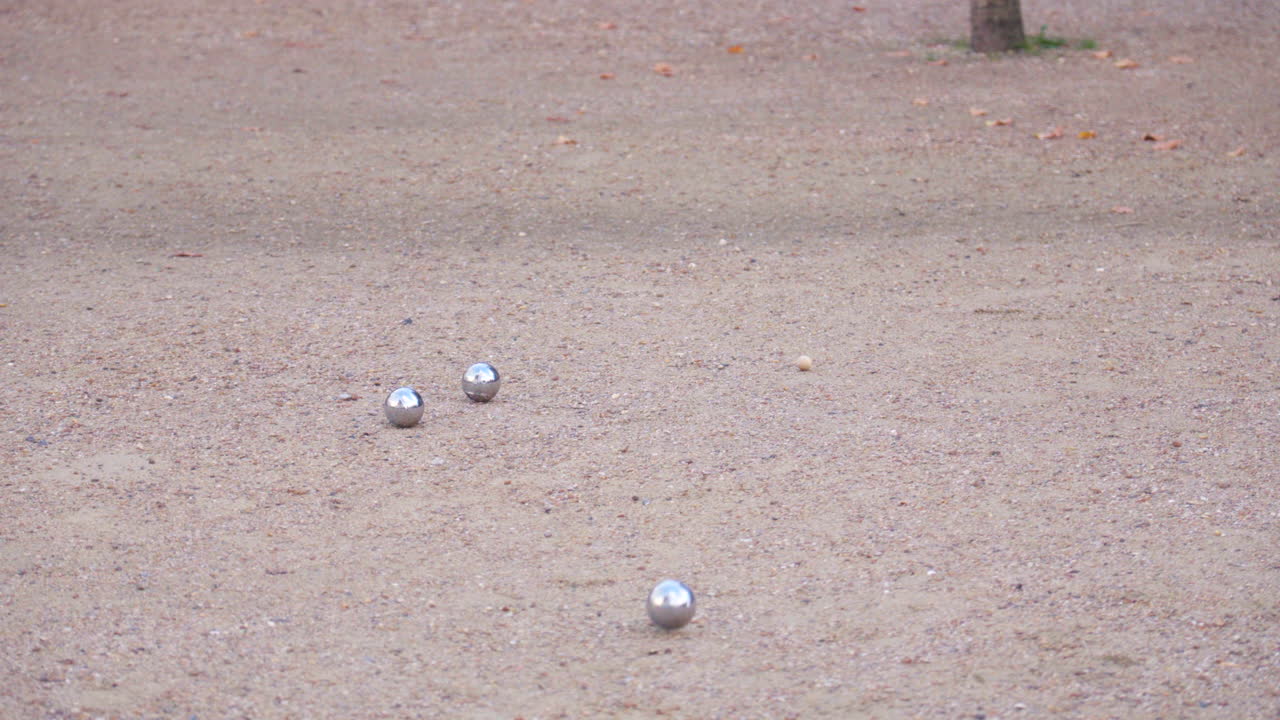 A pétanque ball is thrown and lands as the closest to the cochonnet, amidst several other balls on the ground.