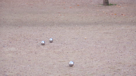 a pétanque ball is thrown and lands as the closest to the cochonnet, amidst several other balls on the ground.