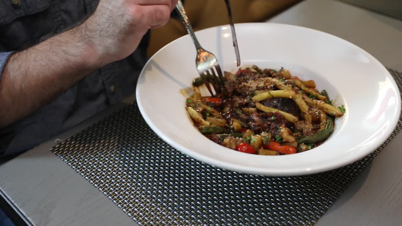 hombre comiendo un plato de pasta con un tenedor y un cuchillo en una mesa gris