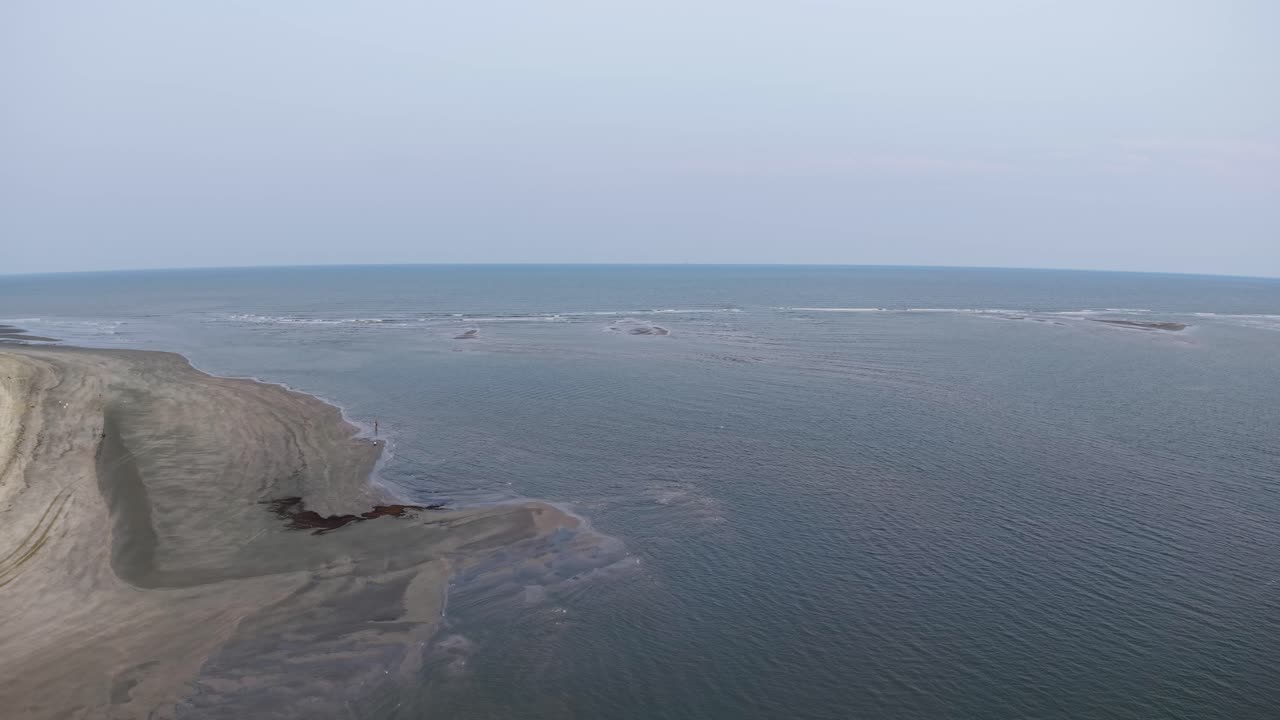 Drone footage of an eroded sandbar and coastal bluff with shallow water channels and pools along the Charleston coastline, showing gentle waves and pale sand under clear sky