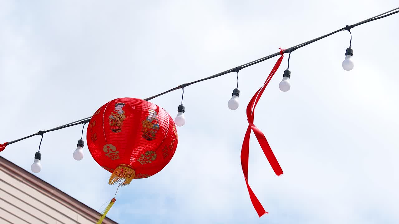 Red Chinese lanterns and ribbons sway gently against a bright sky in Phuket's Old Town, creating a festive atmosphere
