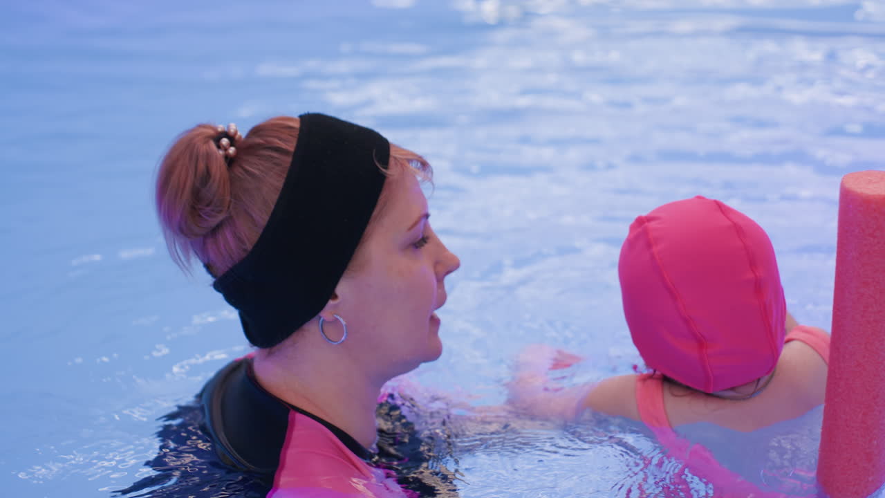 Close up view of white baby diving round with playful movement, enjoying buoyancy in clear pool, sunlight reflections dancing across rippling surface highlighting fun learning moment