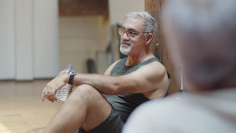 medium shot of cheerful man drinking water after dance class and talking with his friends