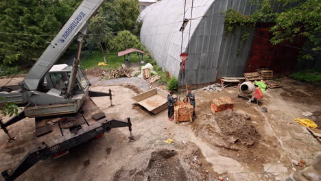 two men attach the pile of red brick pile to the hook of an excavator. a look at the yard of the building under construction.