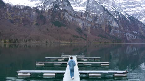 still shot behind a young man walking on a lake pier in the alps, switzerland