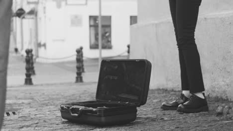 Vista-En-Blanco-Y-Negro-De-Un-Saxofón-En-El-Suelo-Y-Un-Hombre-Con-Chaqueta-Tocando-El-Saxofón-En-La-Calle-1