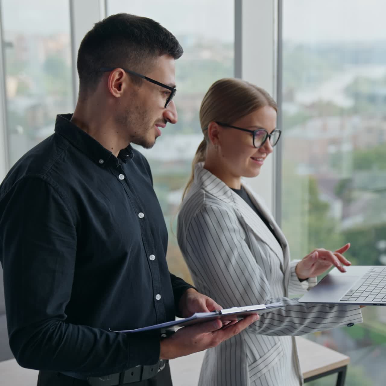 A couple of colleagues standing in office and talking. Positive young people chatting and smiling. Blurred backdrop