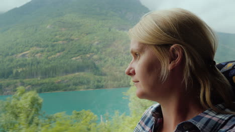 a woman travels by bus in norway looks out the window at the beautiful fjords