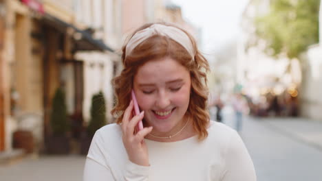 happy young woman having remote conversation talking on smartphone good news gossip in city street