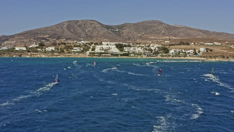 Chrisi-Akti-Paros-Greece-Aerial-v6-cinematic-drone-low-level-flyover-windsurfers-surfing-on-blue-aegean-sea-overlooking-at-beach-and-hillside-resorts-and-holiday-homes---September-2021