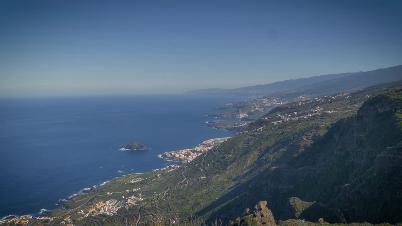 Panoramica di una verde collina che digrada verso il mare azzurro in basso e una piccola città costiera di Tenerife, Isole Canarie