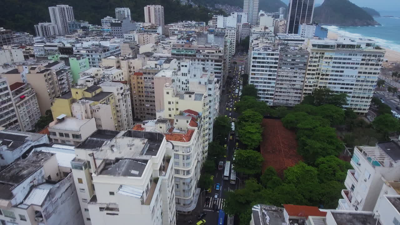 Vista aérea ascendente sobre uma movimentada avenida do Rio com táxis, oceano e montanhas