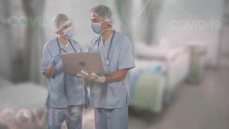 Animation-of-words-Covid-19-floating-over-two-doctors-wearing-face-masks-using-a-laptop