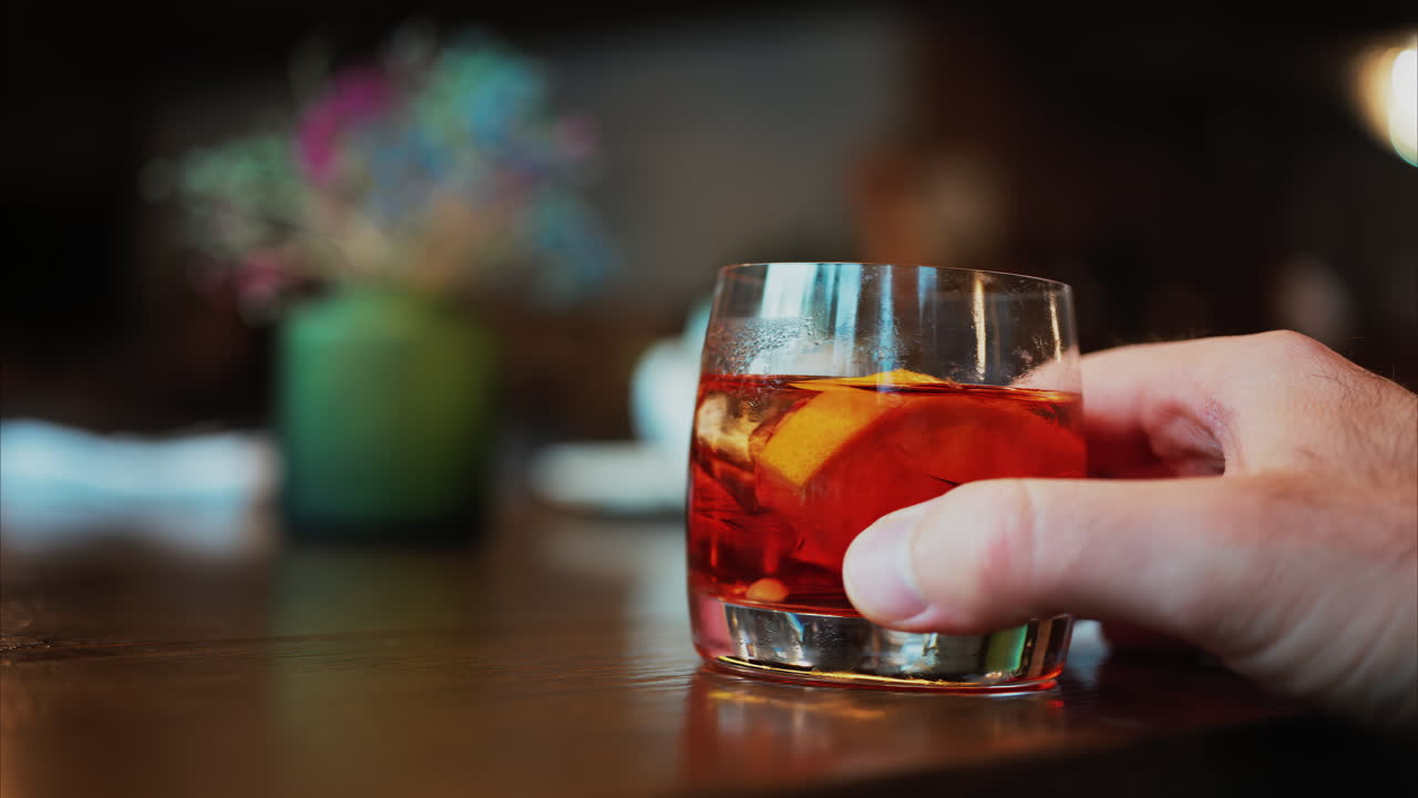 Man's hand holding a glass of Negroni cocktail on a bar counter