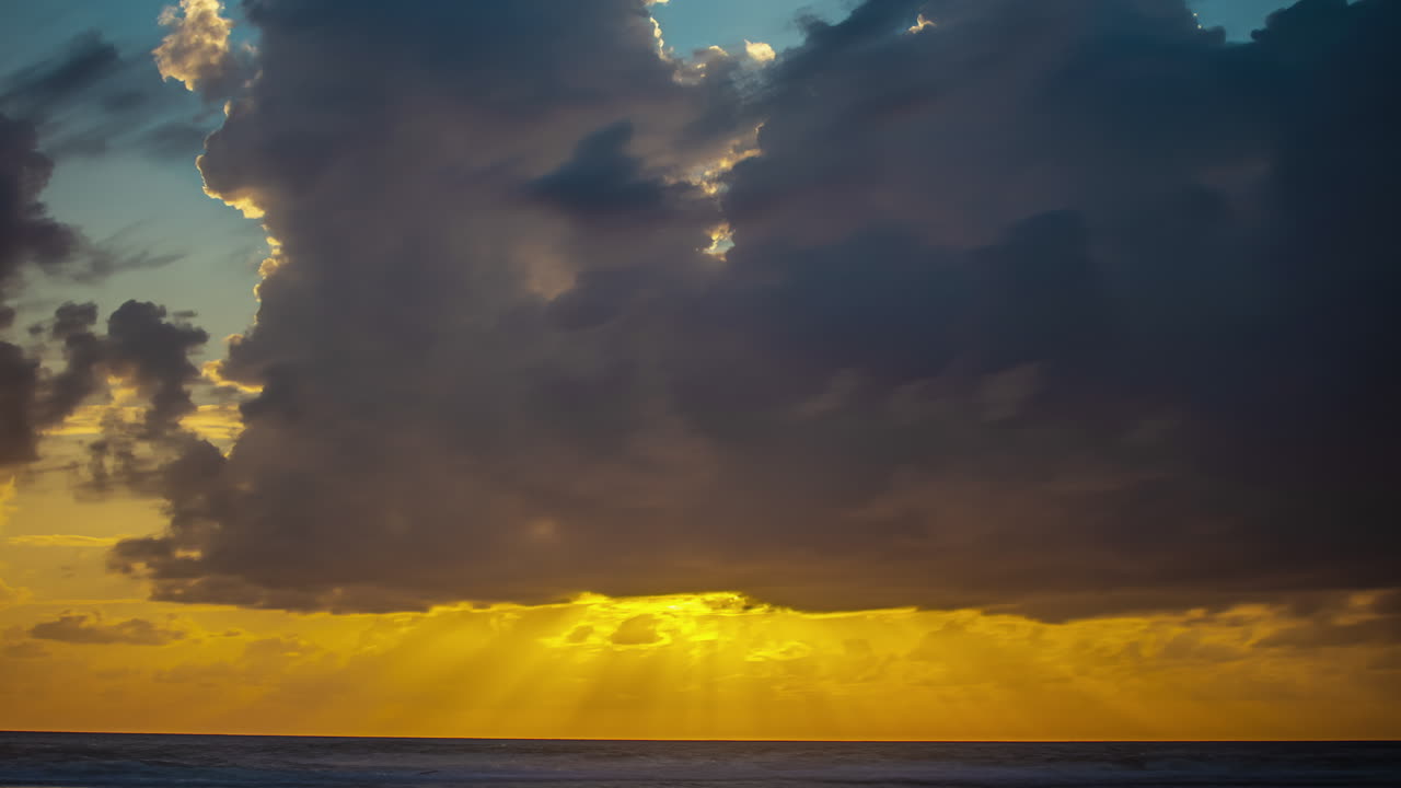 구름 사이로 햇빛이 비치는 바다 위의 일몰 - 극적인 시간 경과
