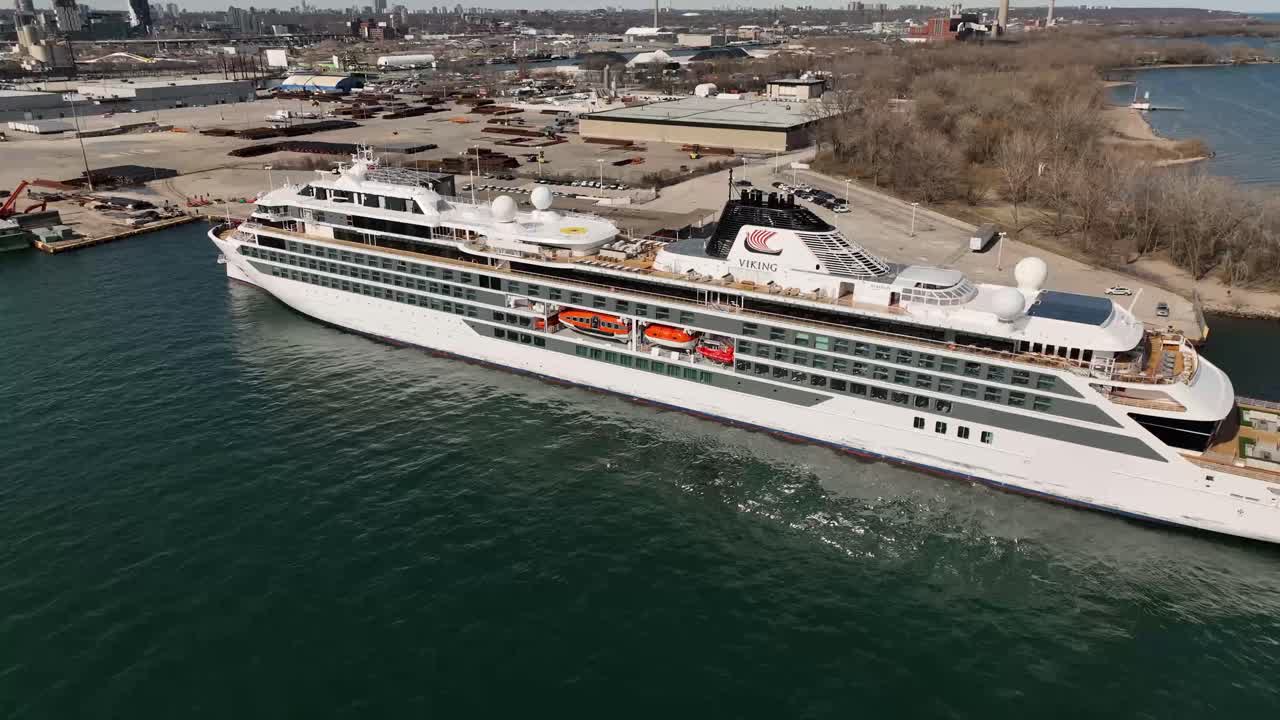 A Viking cruise ship docked in a large port with a city skyline in the background