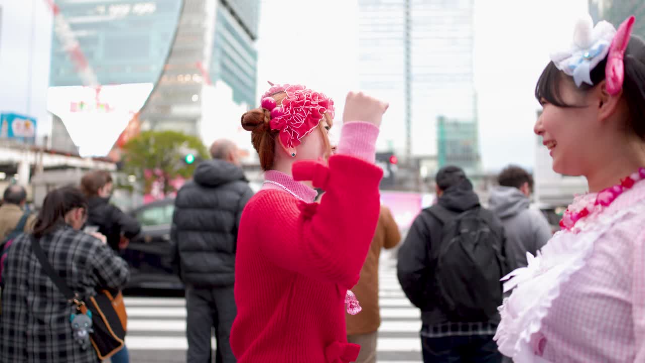 Two young women wearing colorful decora fashion stand and talk on a busy Tokyo street