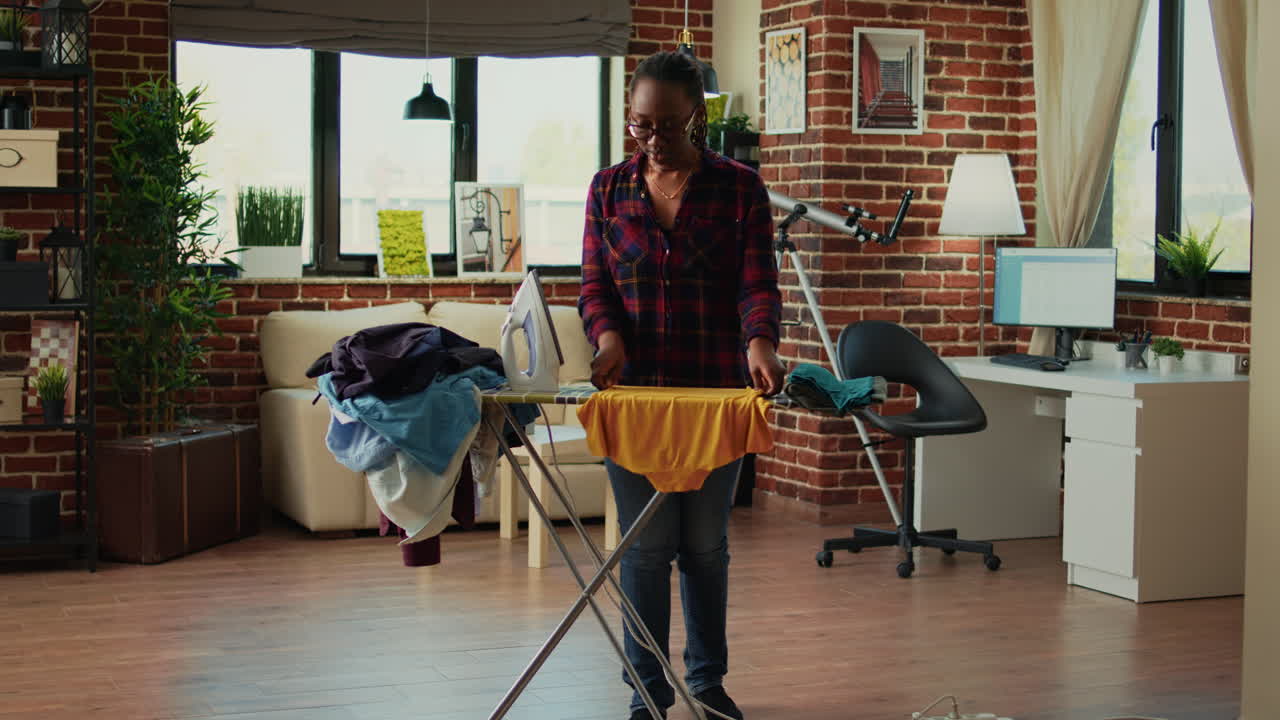 African american housewife using iron on ironing board to do housekeeping work
