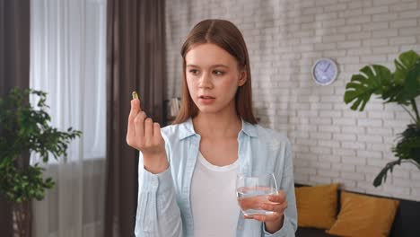 woman taking a vitamin supplement with water at home a woman at home takes a vitamin supplement with a glass of water emphasizing healthy lifestyle choices healthy living concept taking vitamins for skin and hair beauty