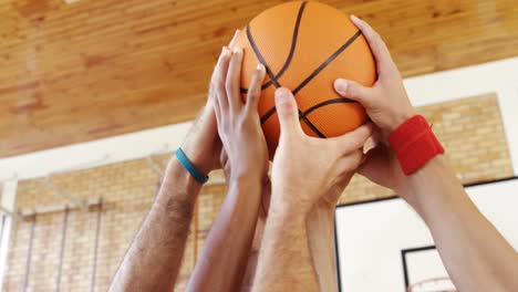 Players-and-coach-holding-basketball-together-in-the-court