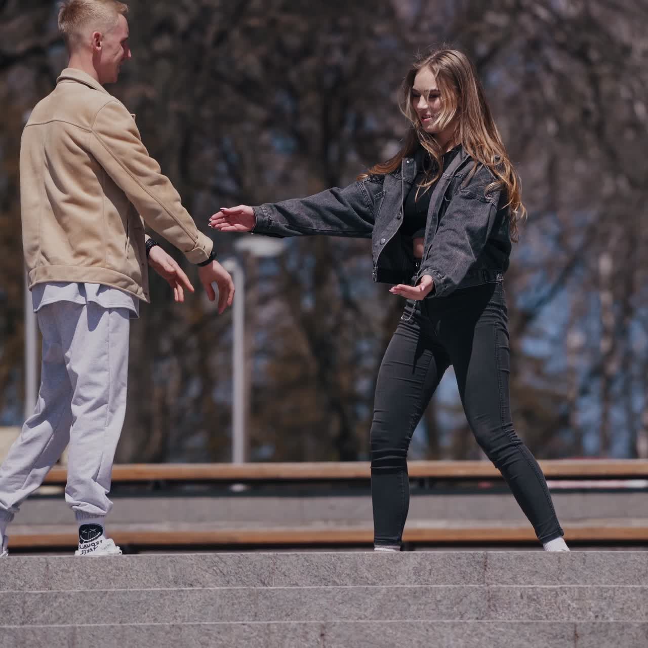 Funny young couple dancing and jumping outdoors. Guy and girl having joy together in the city park in sunny autumn day. Happy relationships concept