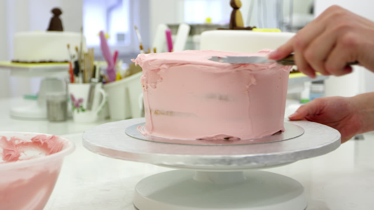 Primo piano di una donna in pasticceria che decora una torta con la glassa.