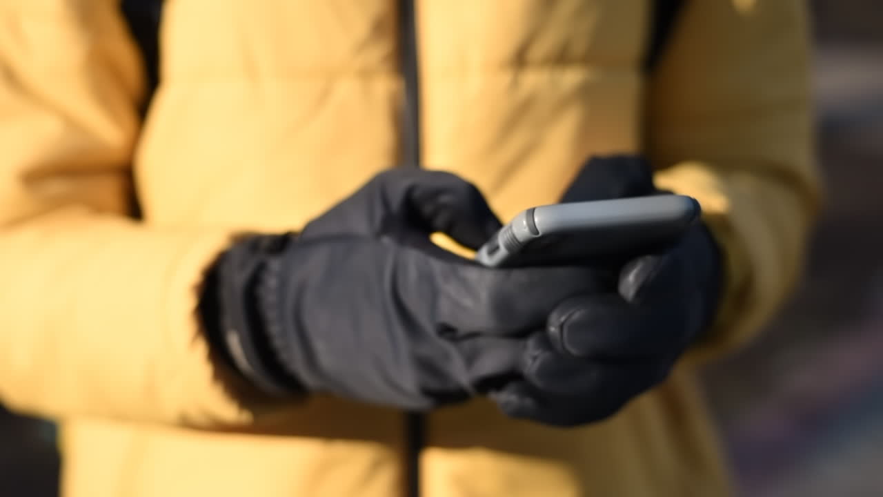 Food delivery man on a scooter in a park using his smartphone. Yellow jacket and black gloves. Winter