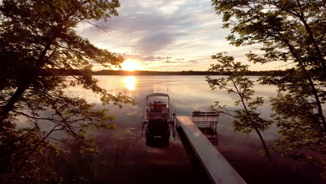 Fliegen-In-Richtung-Angedocktes-Pontonboot-Bei-Sonnenuntergang-Auf-Einem-Reflektierenden-See