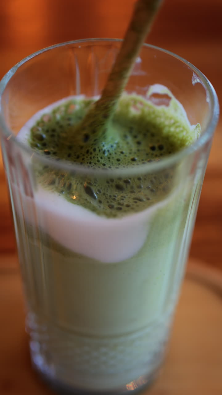 Close up of a spoon mixing in a matcha latte on a table at a cafe. Vertical