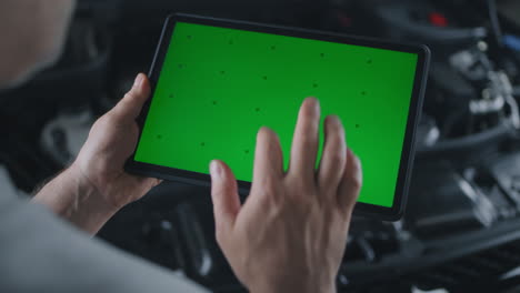 mechanic uses a tablet with a green screen over a car engine