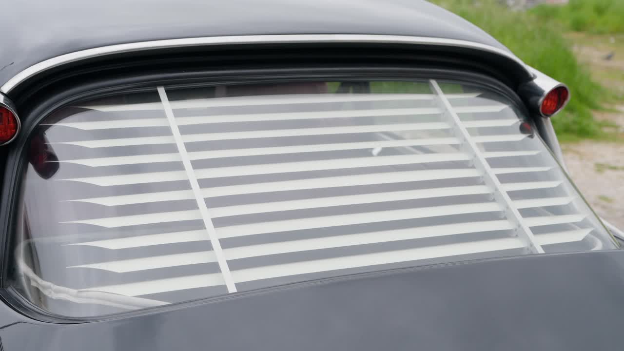 back window of old car featuring striped louvered interior blind
