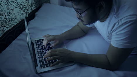 indian man working overtime on his bed at home during night time