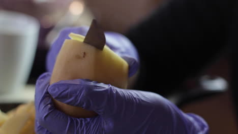 Close-up-of-hands-with-purple-gloves-slicing-potato-into-thin-disks