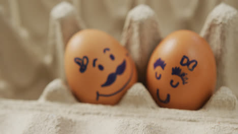 video of close up of two brown eggs with drawn faces in egg carton background