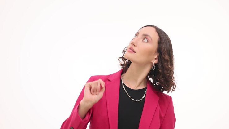 Young Woman in Pink Blazer Pointing Upwards on White Background