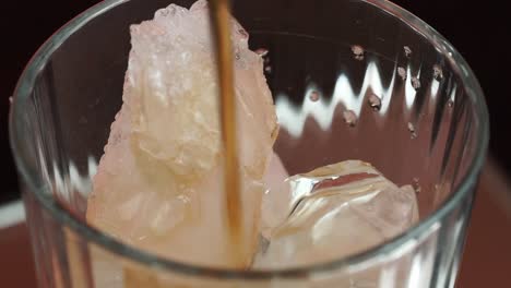 una toma constante del borde superior de un vaso lleno de hielo mientras está lleno de refresco de cola.