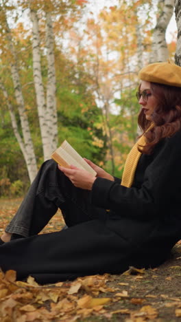 mujer se sienta bajo un árbol en soledad, leyendo un libro pensativamente en el bosque de otoño, rodeada de hojas doradas, abraza la calma, la inspiración y la creatividad