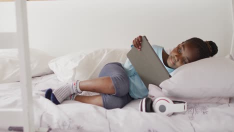 smiling african american girl using tablet lying on bunk bed at home, copy space