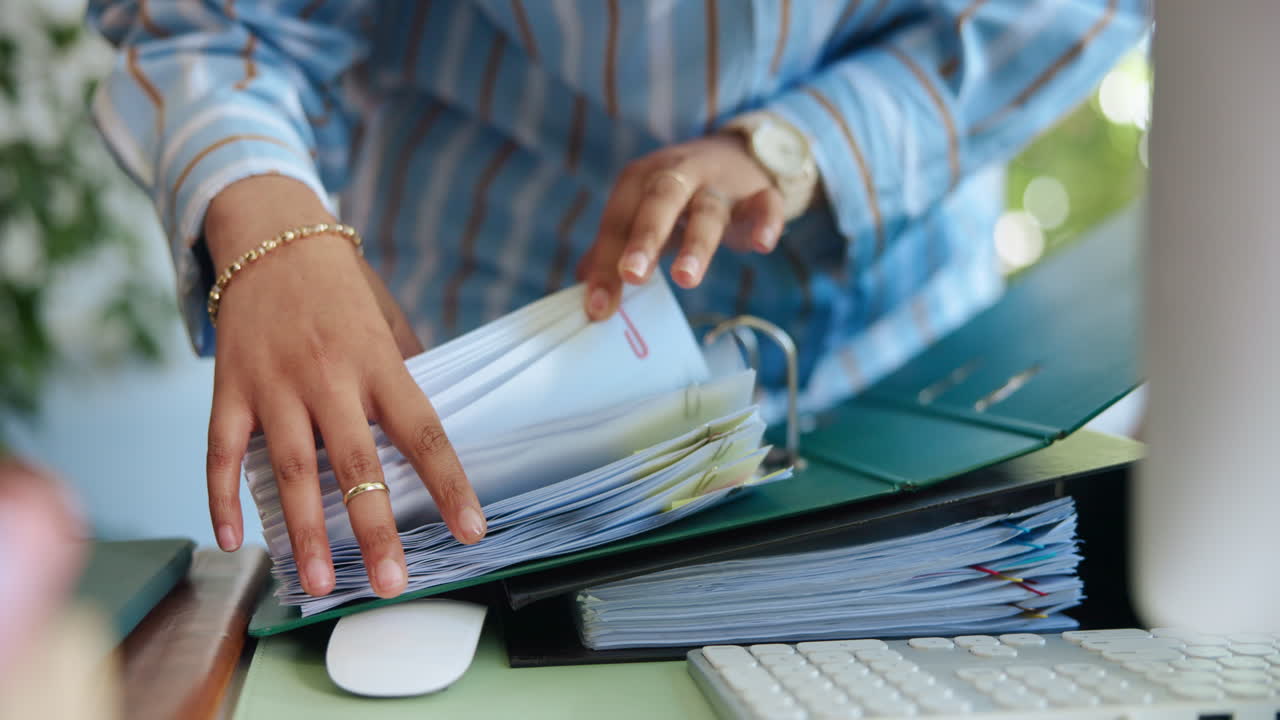 Person Organizing Documents in a Green Binder on an Office Desk