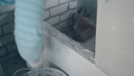brazo de trabajador en guantes sostiene cuchillo de masilla y manchas pared